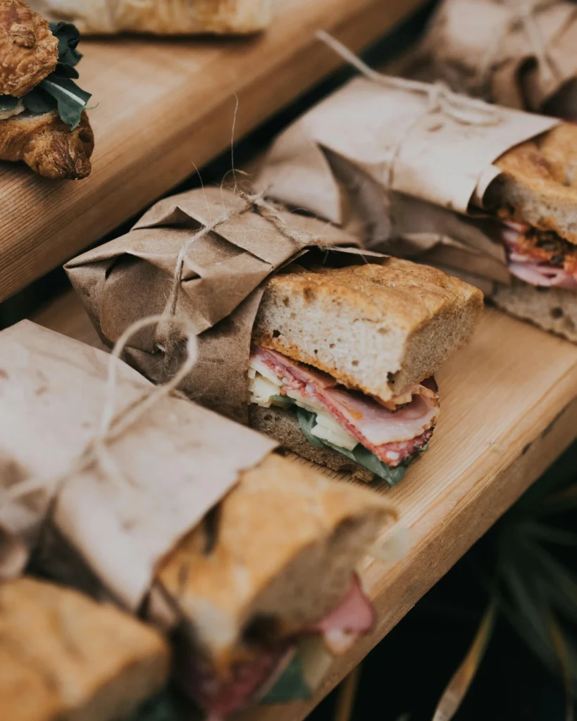 Half verpakte broodjes met sla, kaas en vlees in papieren zak met touw, geïnspireerd op jaren 40 lunches.
