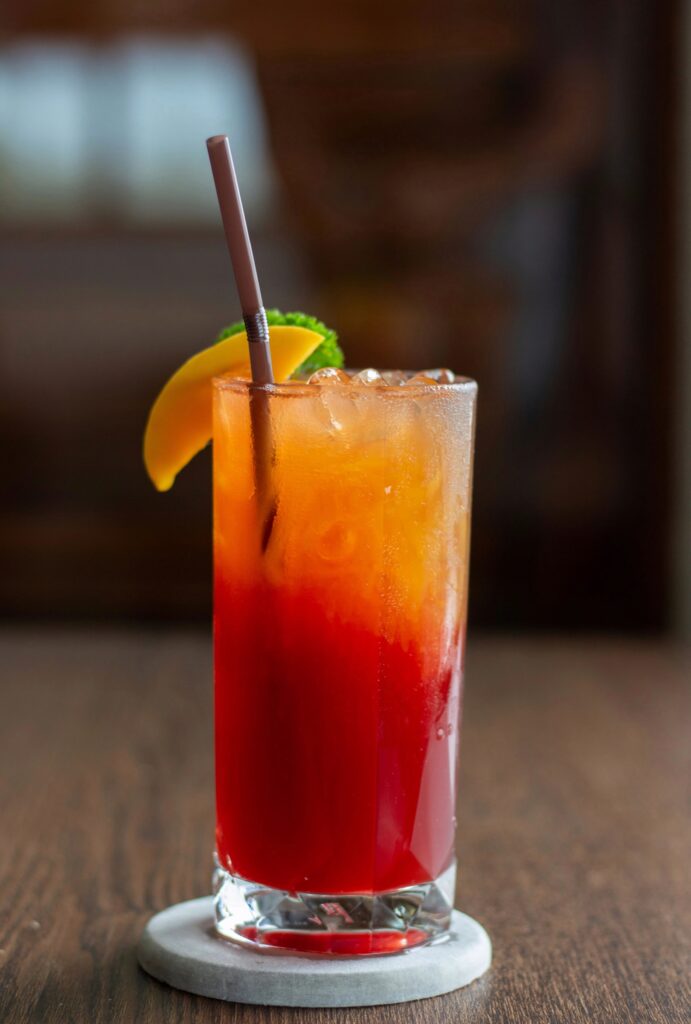 Glas met Tequila Sunrise cocktail, afgetopt met fruit op de rand en een rietje, typische jaren 80 cocktail.