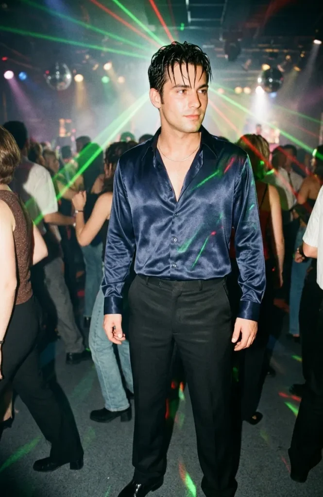 Man in glanzend satijnen overhemd en zwarte broek tijdens een stijlvol eind jaren 90 feest met club en popinvloeden.